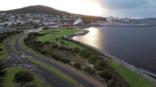 Aerial view of Albany's waterfront parkland and Princess Royal Harbour, with the town and a hill behind.