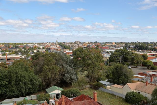 Ballarat city skyline with the Town Hall clock tower and church spires above trees and old rooftops.