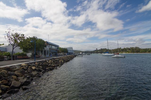 The rock-lined riverside walk at Batemans Bay beside the Clyde River, with moored yachts and the old lift bridge in the distance.