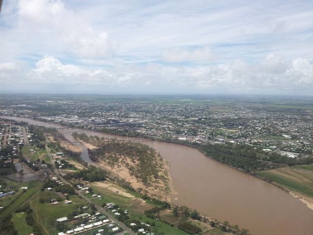 Aerial view of Bundaberg beside the brown, flood-swollen Burnett River, with its bridges and the city spreading out behind.