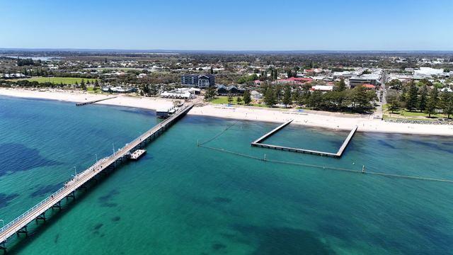 Aerial view of the Busselton Jetty reaching out over turquoise water from the town's beachfront.