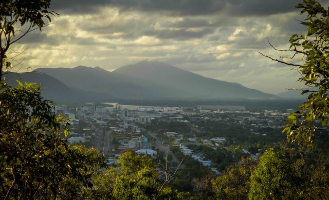 Early-morning view over Cairns city towards Trinity Inlet and the ranges, framed by trees on Mount Whitfield.
