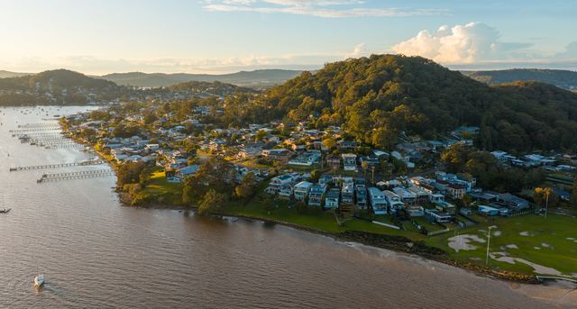 Aerial view of waterfront homes and jetties on Brisbane Water near Gosford at sunset.