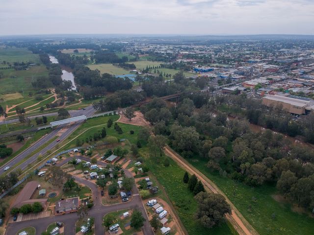 Aerial view of Dubbo with the Macquarie River, the old rail bridge and the city centre beside green parkland.