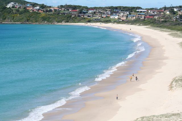 The curve of One Mile Beach at Forster, with turquoise water and hillside homes behind.