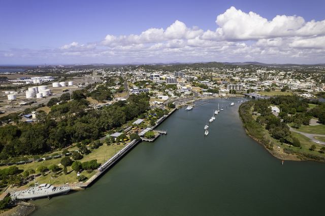 Aerial view of Gladstone's East Shores parkland and Auckland Creek leading to the city centre, with the harbour and industry behind.