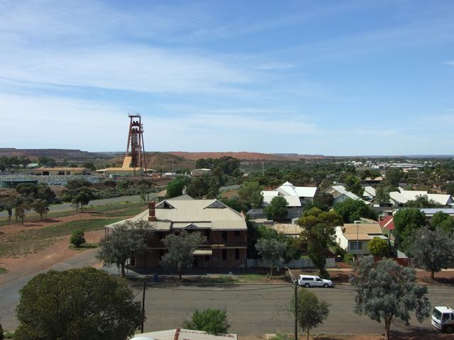 View over Kalgoorlie's houses and streets towards a mine headframe and red mullock heaps.