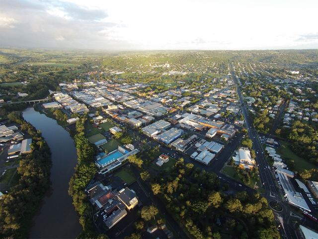 Aerial view of Lismore's city centre beside the Wilsons River, lit by low golden light with green hills beyond.