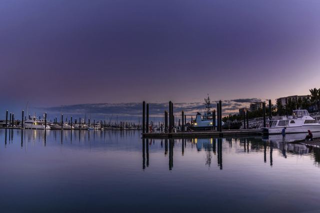 Boats moored at Mackay Harbour marina at dusk under a purple sky, with apartments and palm trees on the right.
