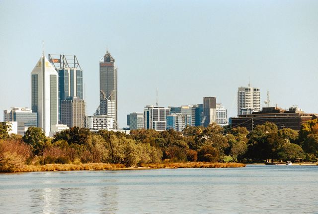 Perth city skyline seen across the Swan River with trees along the foreshore.