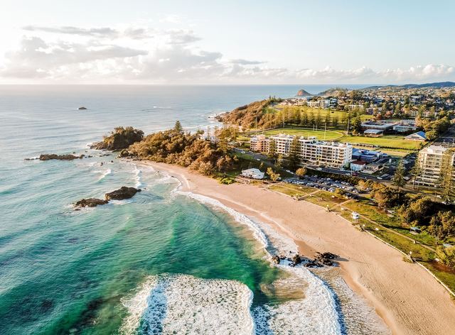 Aerial view of Port Macquarie's Town Beach, rocky headland and beachfront apartments in morning light.