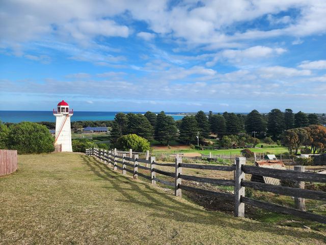 The Flagstaff Hill lighthouse in Warrnambool, with Norfolk pines, parkland and the ocean beyond.