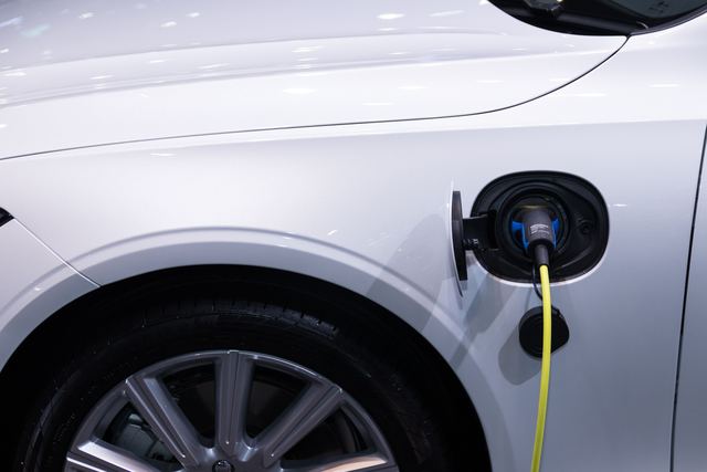 Close-up of a charging cable plugged into the charge port on the front wing of a white electric car.