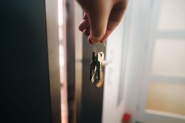 A hand holding a ring of house keys in front of an open front door.