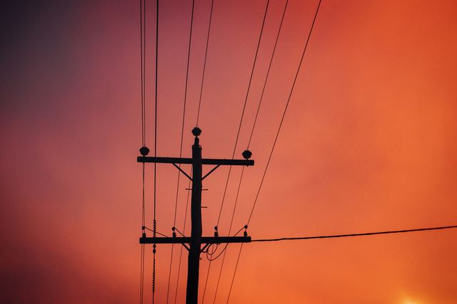 A timber power pole with two crossarms, insulators and overhead lines silhouetted against an orange sunset sky.