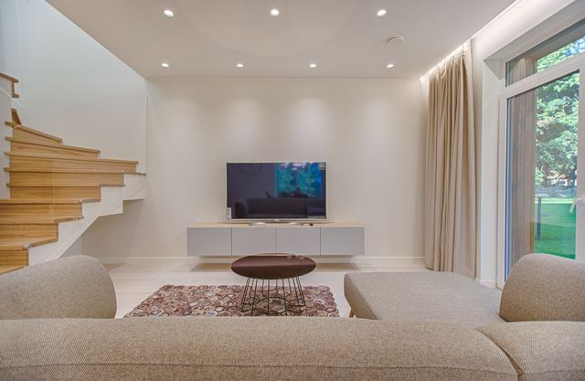 A living room with rows of round LED downlights in a white ceiling above a sofa and TV unit.