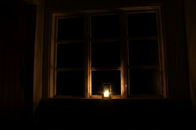 A dark room with a single candle lantern glowing on a window sill.