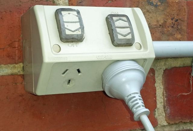 A weatherproof Australian double power point on a brick wall with a lead plugged in.