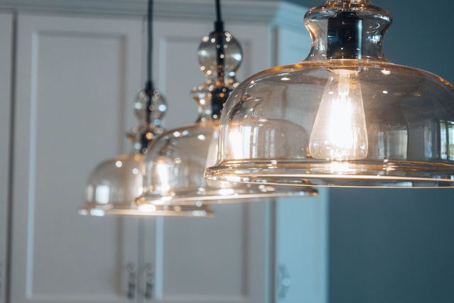 A row of three clear glass pendant lights with filament bulbs hanging in a kitchen.
