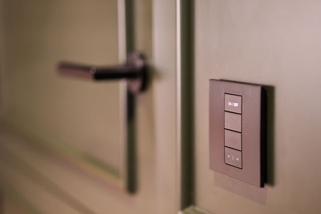 A smart lighting keypad with an on/off button and dimmer arrows on the wall beside a door handle.