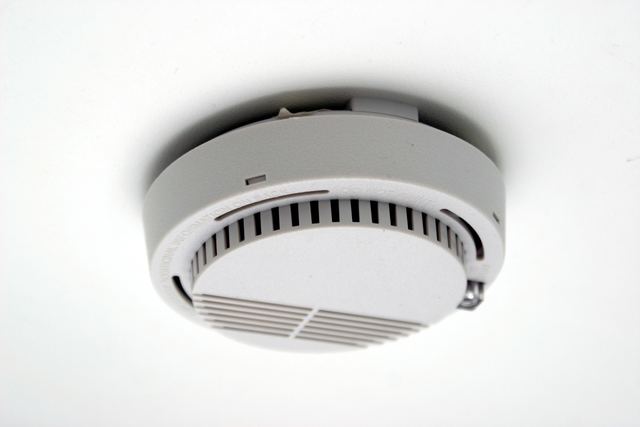 A white smoke alarm mounted on a plain white ceiling, seen from below.