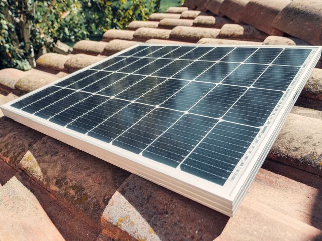 A solar panel resting on terracotta roof tiles in sunshine.