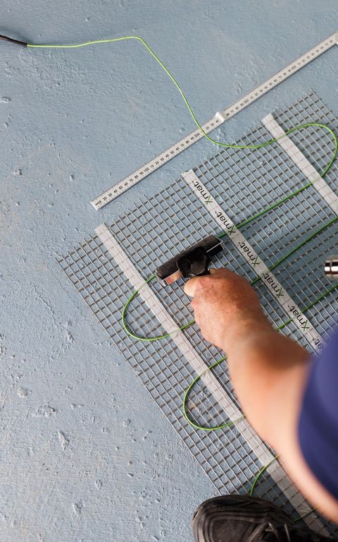 Heating mat being laid out on a waterproofed bathroom floor, before the tiles go down