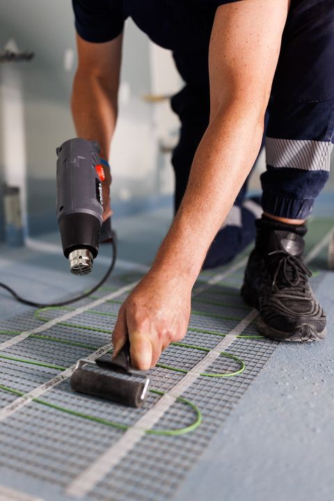Rolling a heating mat flat so it sits evenly under the tiles